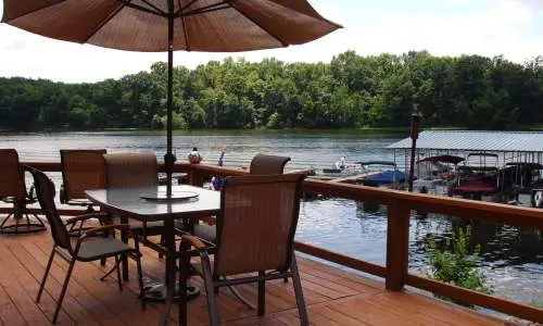 Eine Terrasse mit Stühlen und Sonnenschirm mit Blick auf einen See, an dem Boote angedockt sind