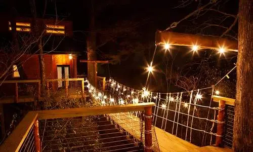 Eine hölzerne Brücke zu einer mit Lichterketten beleuchteten Baumhaushütte