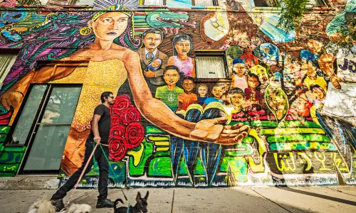 Ein Mann geht mit drei Hunden vor einer bunten Wandmalerei spazieren.