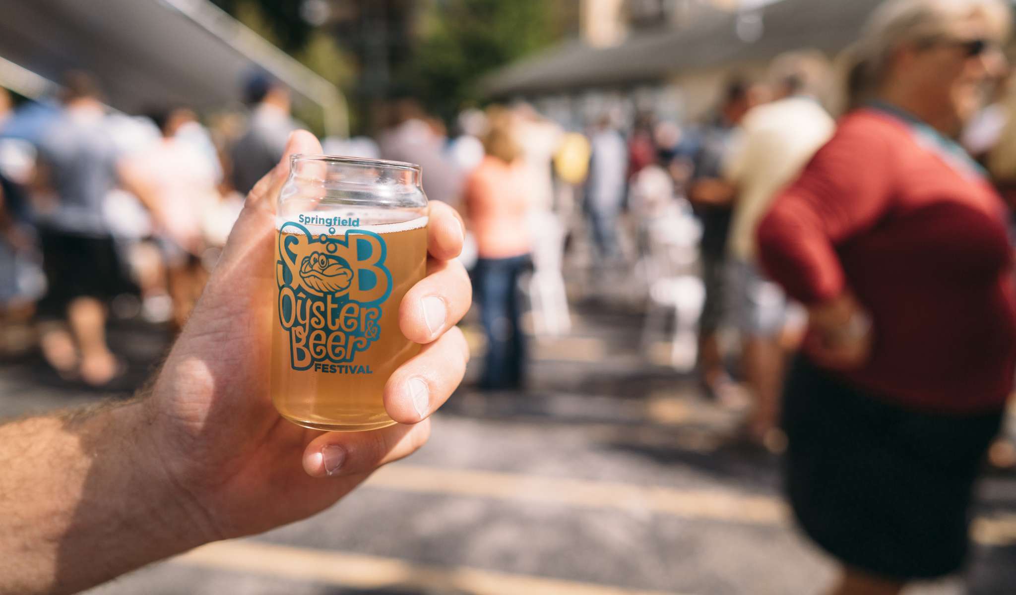 Jemand hält ein mit Bier gefülltes Glas der Marke Springfield Oyster and Beer Festival in der Hand.