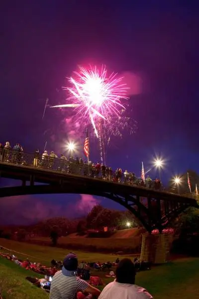 Menschen sitzen in einem Park an einer Brücke und beobachten ein Feuerwerk am Himmel