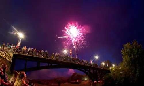 Menschen sitzen in einem Park an einer Brücke und beobachten ein Feuerwerk am Himmel