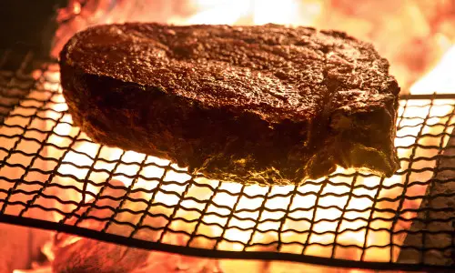 Ein großes Steak, das auf einem Drahtgestell über offener Flamme gebraten wird