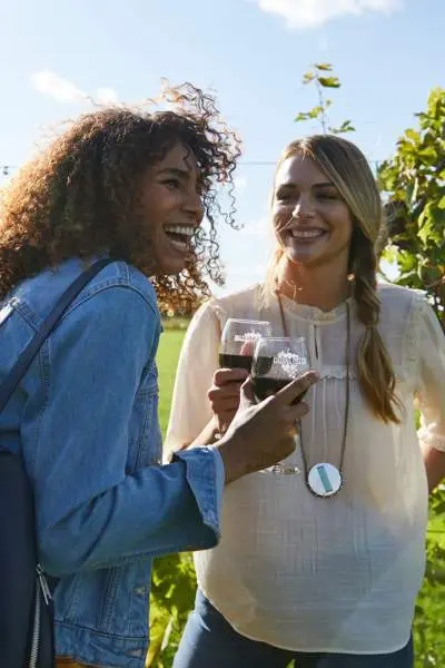 Zwei Mädchen lachen, während sie auf einem Weinberg Rotwein genießen