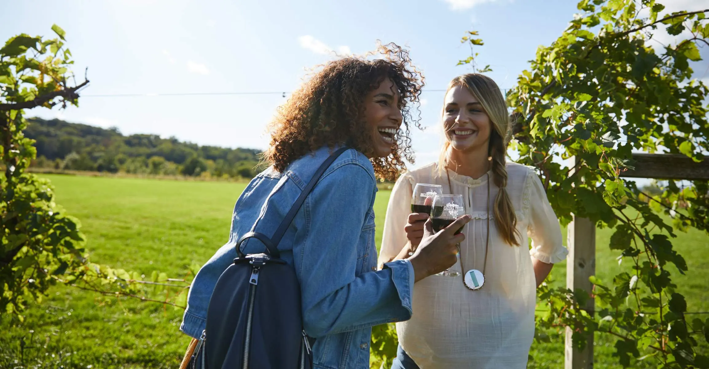 Zwei Mädchen lachen, während sie auf einem Weinberg Rotwein genießen