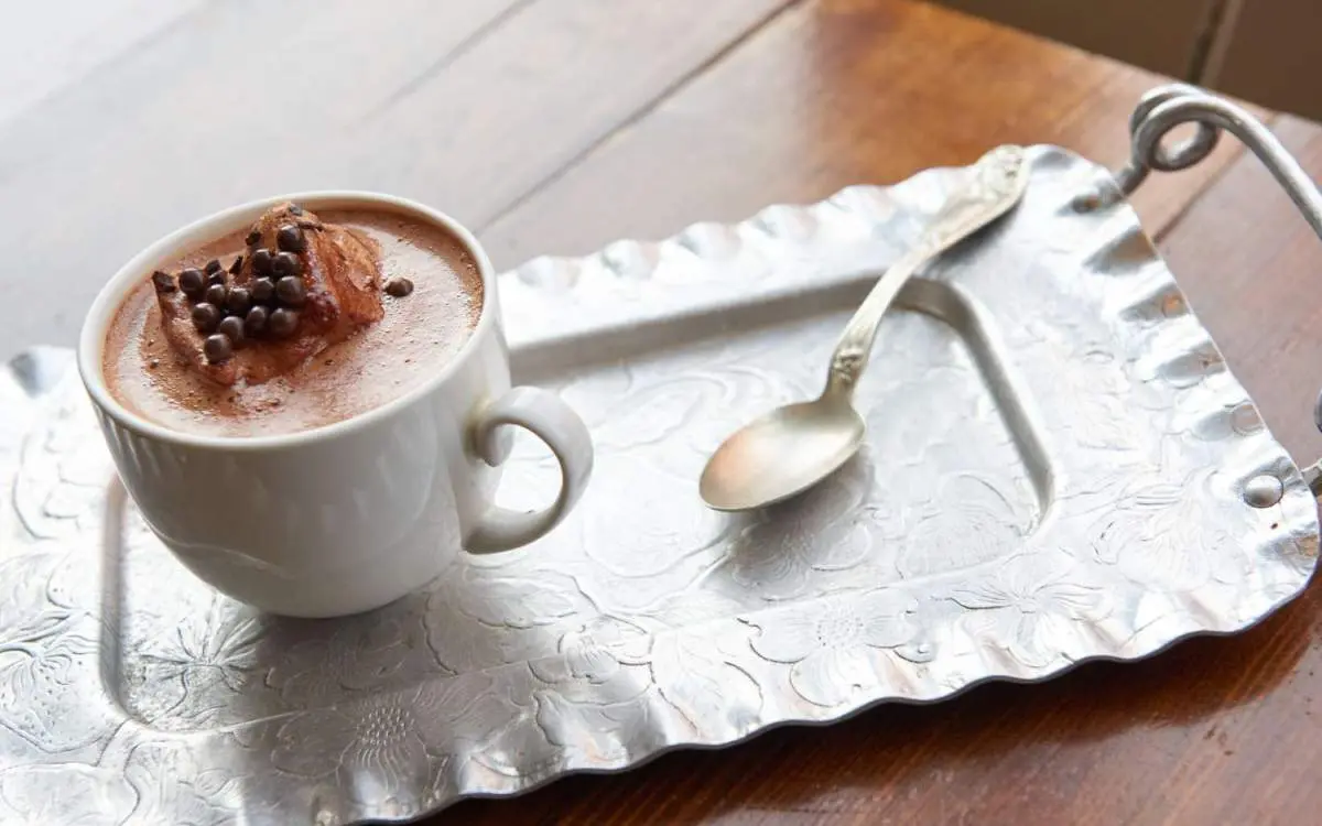 Ein Becher mit heißer Schokolade und ein Teelöffel auf einem Serviertablett