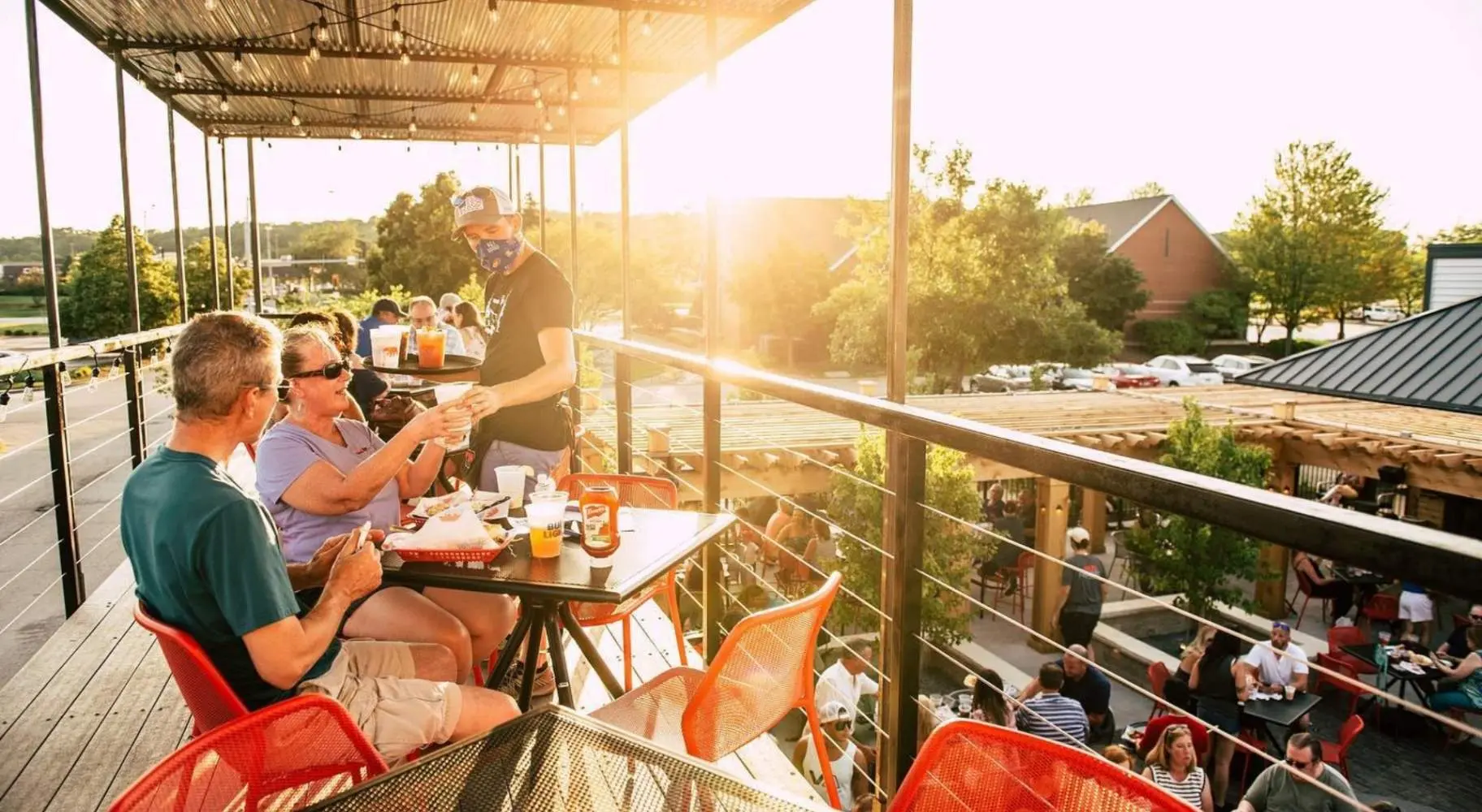 Menschen, die auf einer sonnenüberfluteten Empore in einem Restaurant im Freien bedient werden