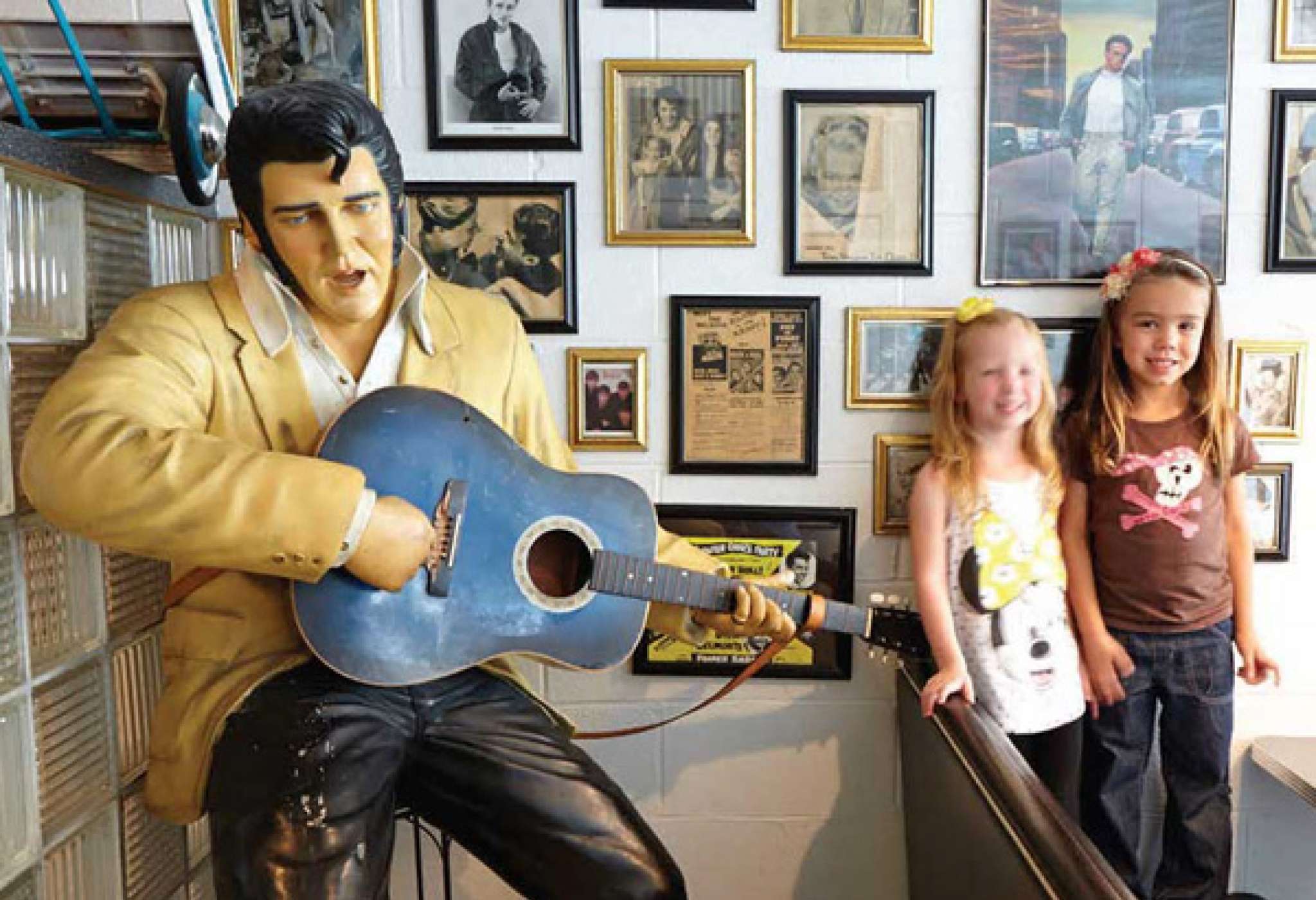 Zwei junge Kinder lassen sich neben einer Statue von Elvis Presley mit einer Gitarre fotografieren 