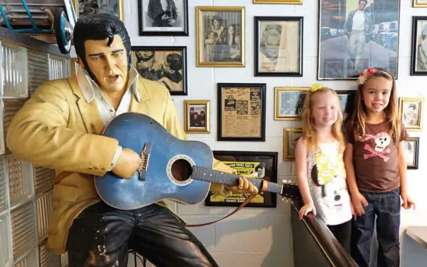 Zwei junge Kinder lassen sich neben einer Statue von Elvis Presley mit einer Gitarre fotografieren