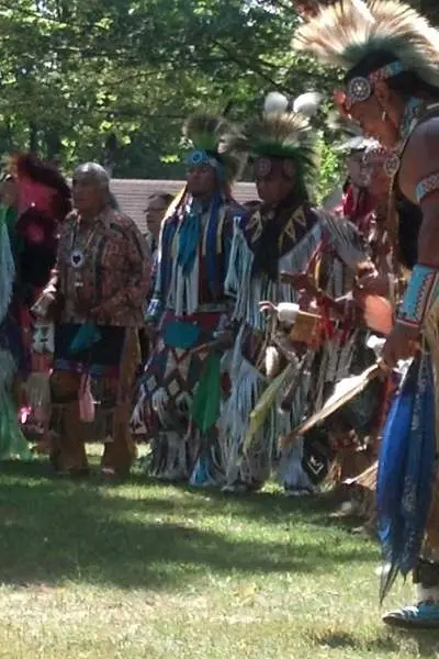 Eine Gruppe von Männern in indianischer Kleidung auf einer Graslichtung inmitten von Bäumen