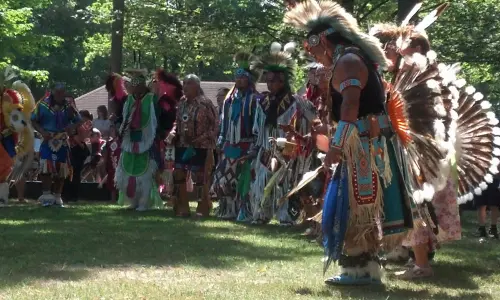 Eine Gruppe von Männern in indianischer Kleidung auf einer Graslichtung inmitten von Bäumen