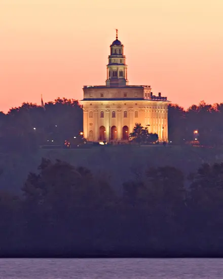 Ein beleuchteter Tempel hinter Bäumen und einem Fluss