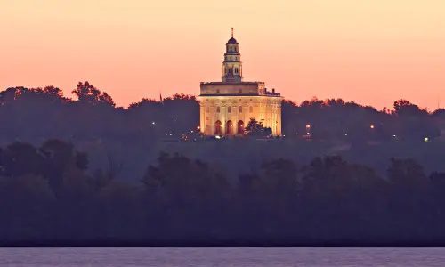 Ein beleuchteter Tempel hinter Bäumen und einem Fluss