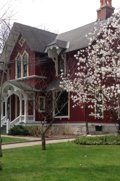 Ein prächtiges, zweistöckiges, rotes Holzhaus aus dem 19. Jahrhundert, hinter einem Rasen und einem blühenden Baum