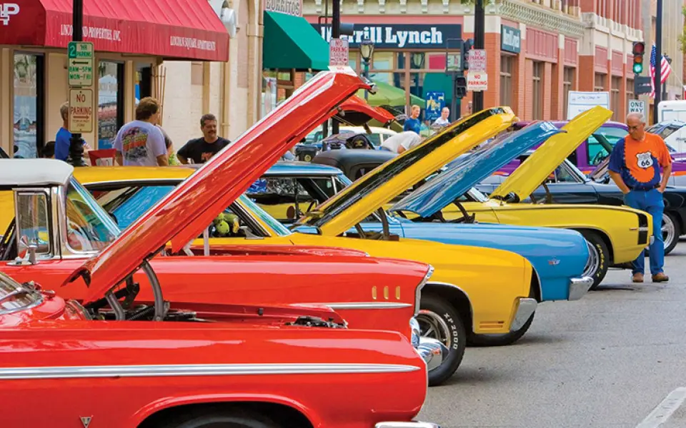 Bunte Oldtimer mit hochgeklappten Motorhauben säumen während einer Route-66-Oldtimerschau eine Straße in der Innenstadt.