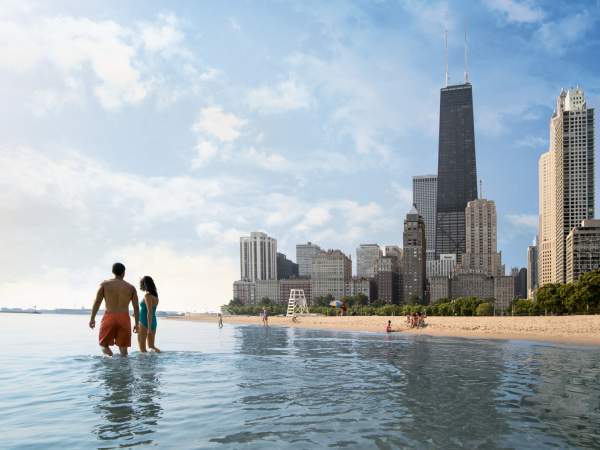 Ein Paar, das durch die Untiefen des Michigansees neben einem Sandstrand spaziert, mit Wolkenkratzern im Hintergrund