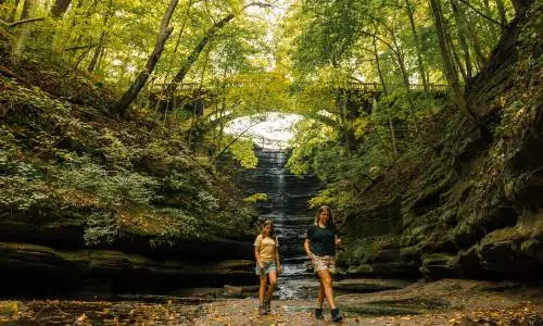 Zwei Mädchen spazieren vor einem Wasserfall im Matthiessen State Park