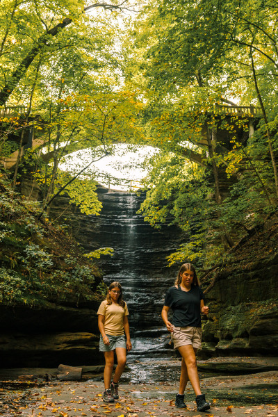 Zwei Mädchen spazieren vor einem Wasserfall im Matthiessen State Park