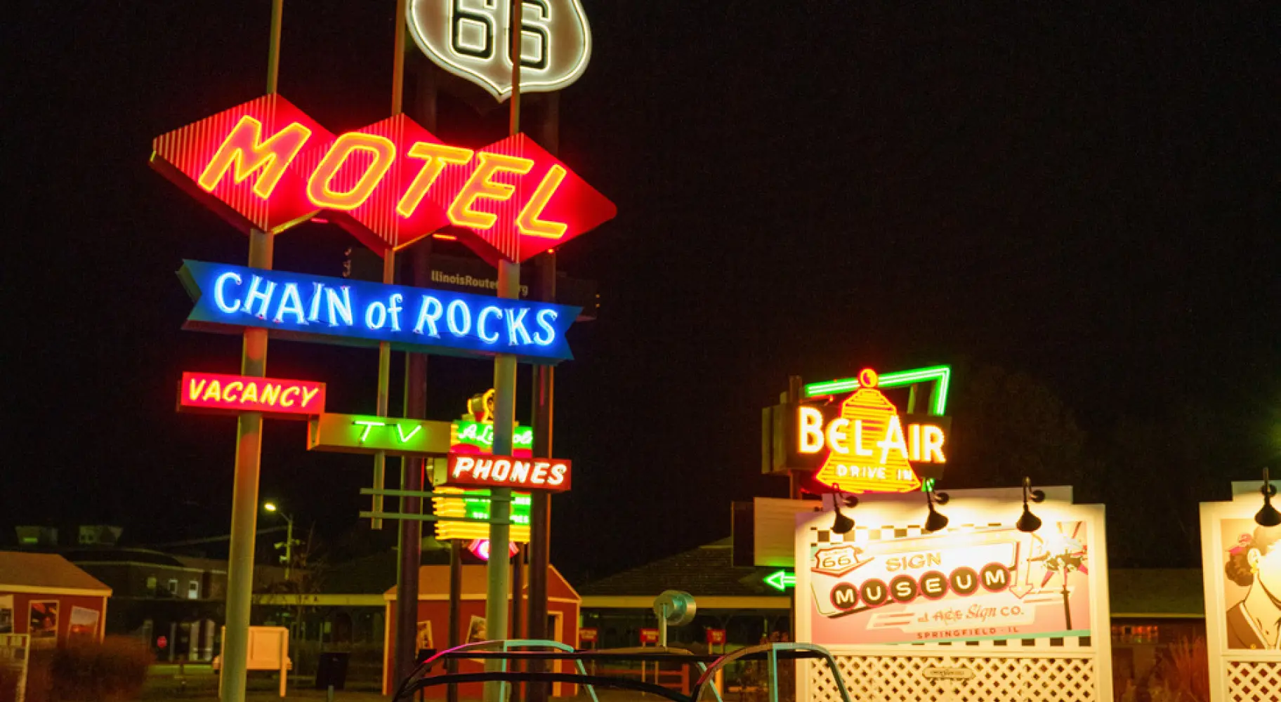 Vintage-Neon-Schilder von Route-66-Motels und ein klassisches Tretauto, die nachts beleuchtet sind.