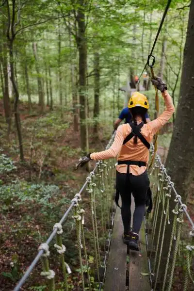 Menschen auf einer Brücke, die die Wälder mit Gurten und Sicherheitshelmen bei Canopy Tours überqueren.