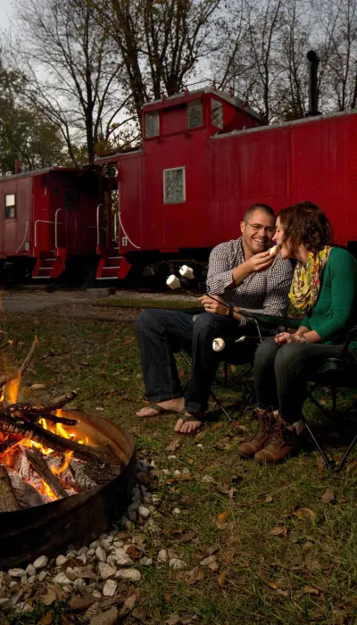 Ein Paar röstet Marshmallows am Lagerfeuer mit einem Zug im Rücken.