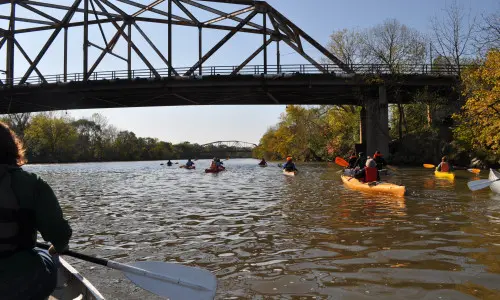 Eine Gruppe von Menschen paddelt in Kanus den Fluss hinunter