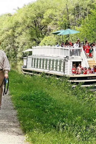 Eine Frau geht mit ihrem Pferd am Kanal entlang, während das I&M-Kanalboot vorbeifährt