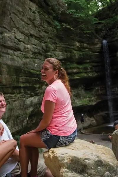 Eine vierköpfige Familie ruht sich auf Felsen vor einem Wasserfall aus