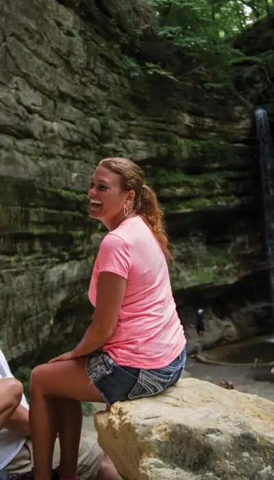 Eine vierköpfige Familie ruht sich auf Felsen vor einem Wasserfall aus