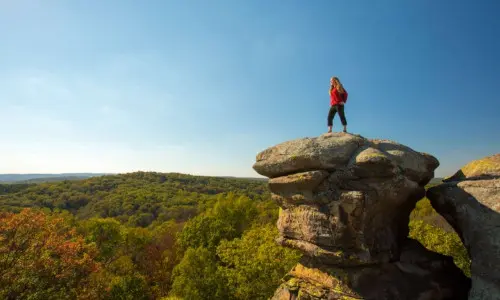 Wanderer auf dem Gipfel eines großen Felsens mit Blick auf den Wald.