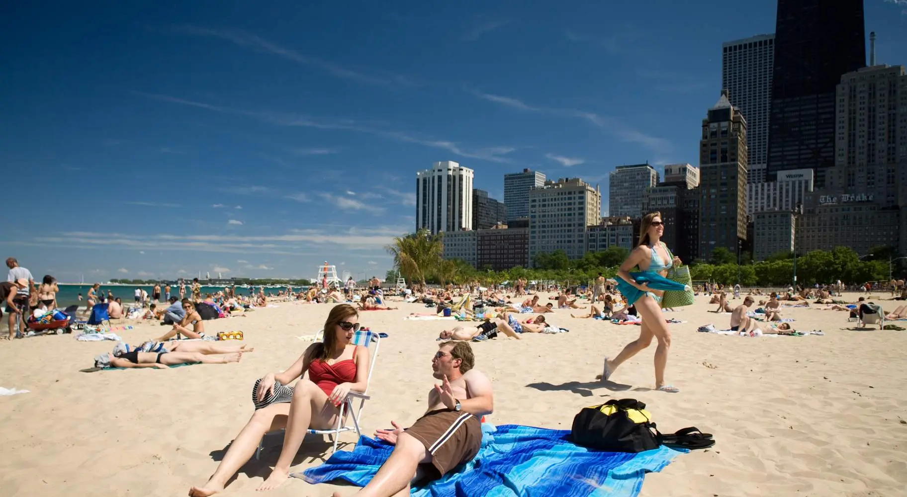 Zwei Menschen liegen auf einem Sandstrand, mit Menschenmengen im Hintergrund und der Skyline von Chicago