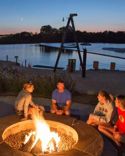 Vier Personen, die in der Abenddämmerung am Strand eines Sees um ein Feuer sitzen