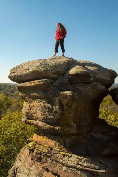 Frau steht auf einem großen Felsen mit Blick auf den Wald