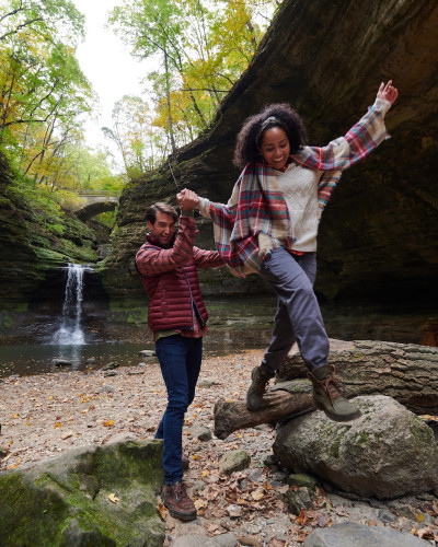 Zwei Personen klettern auf Felsen vor einem Wasserfall