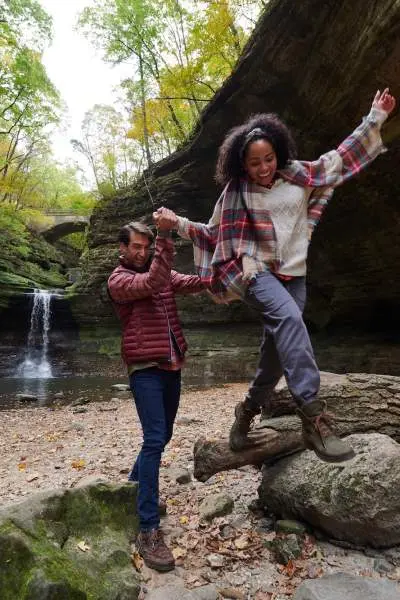 Zwei Personen klettern auf Felsen vor einem Wasserfall