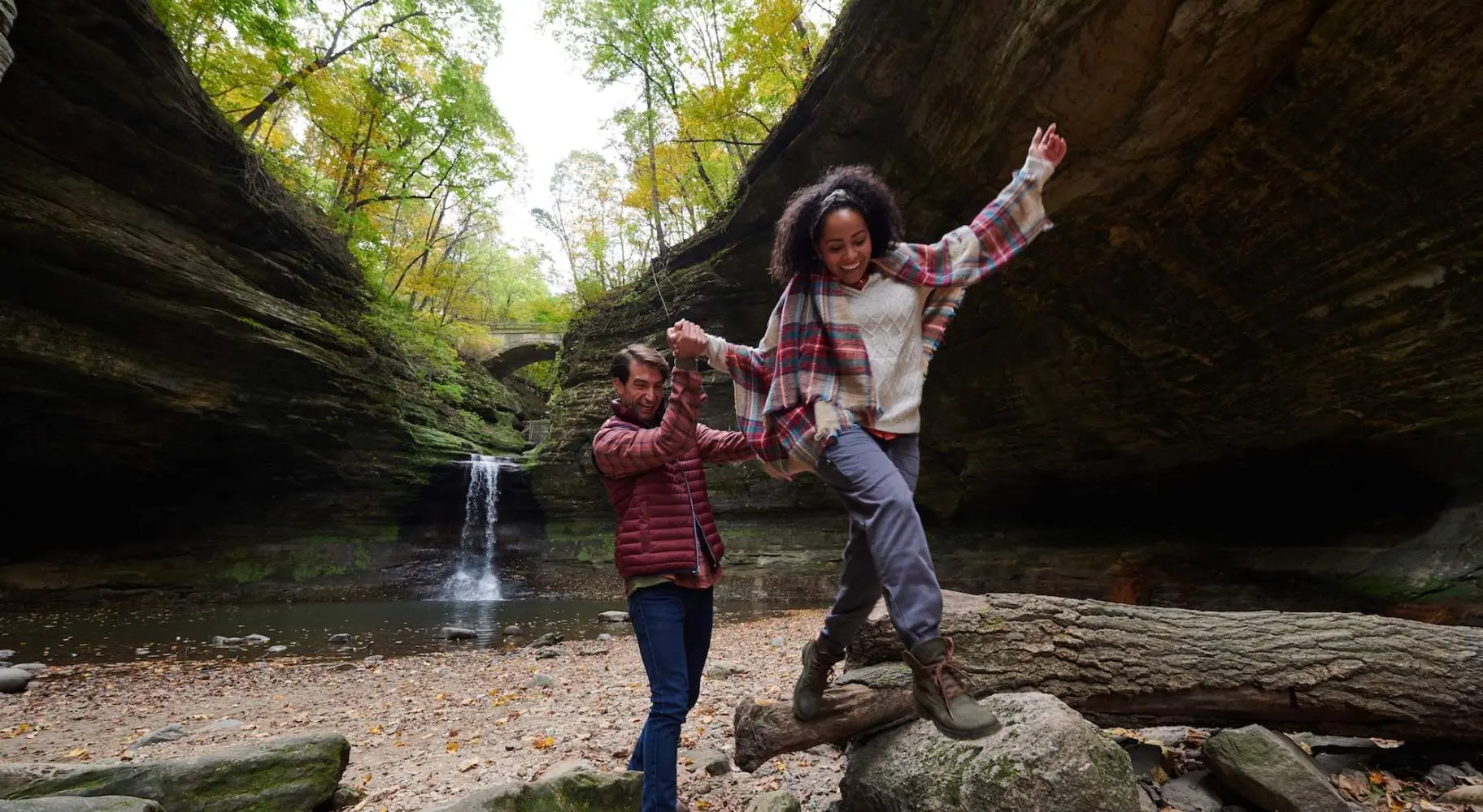 Zwei Personen klettern auf Felsen vor einem Wasserfall