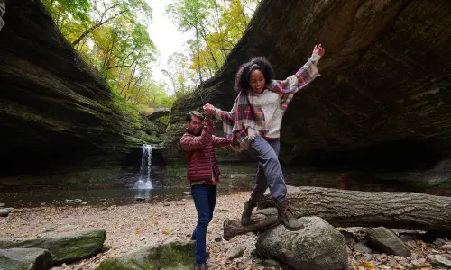 Zwei Personen klettern auf Felsen vor einem Wasserfall