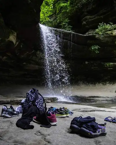 Ein Wasserfall von einem Felsen, mit Taschen und Schuhen, die unten auf dem Felsen liegen