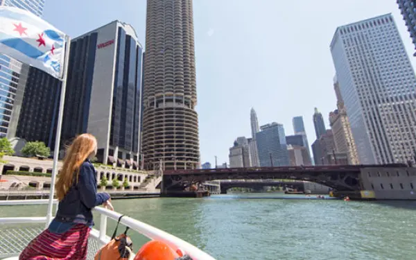 Eine Frau lehnt an der Reling eines Flusskreuzfahrtschiffs auf dem Chicago River und blickt auf die Gebäude der Stadt.