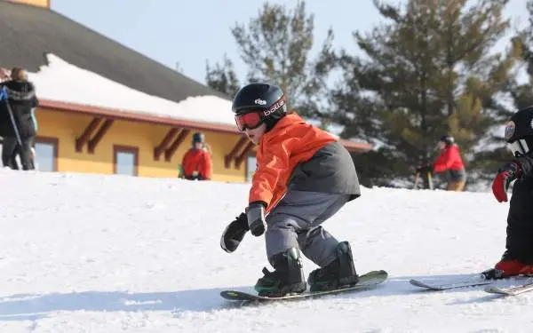 Ein kleines Kind fährt auf einem Snowboard durch den Schnee, trägt einen Helm, eine Brille und warme Skikleidung