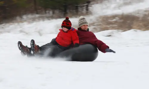 Ein Mann und ein Junge beim Snowtubing auf dem Mount Hoy