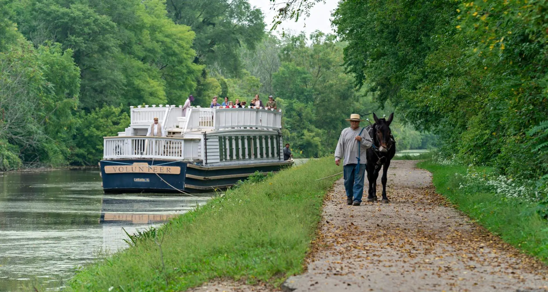 Ein Boot, das den Fluss hinunterfährt, und ein Mann, der mit einem Maultier einen Weg entlangläuft