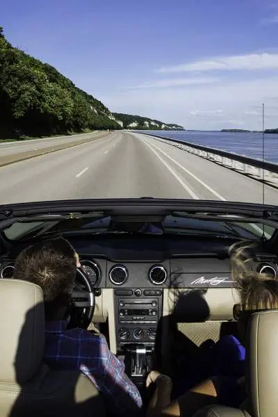 Zwei Personen fahren in einem Auto ohne Dach eine Straße entlang