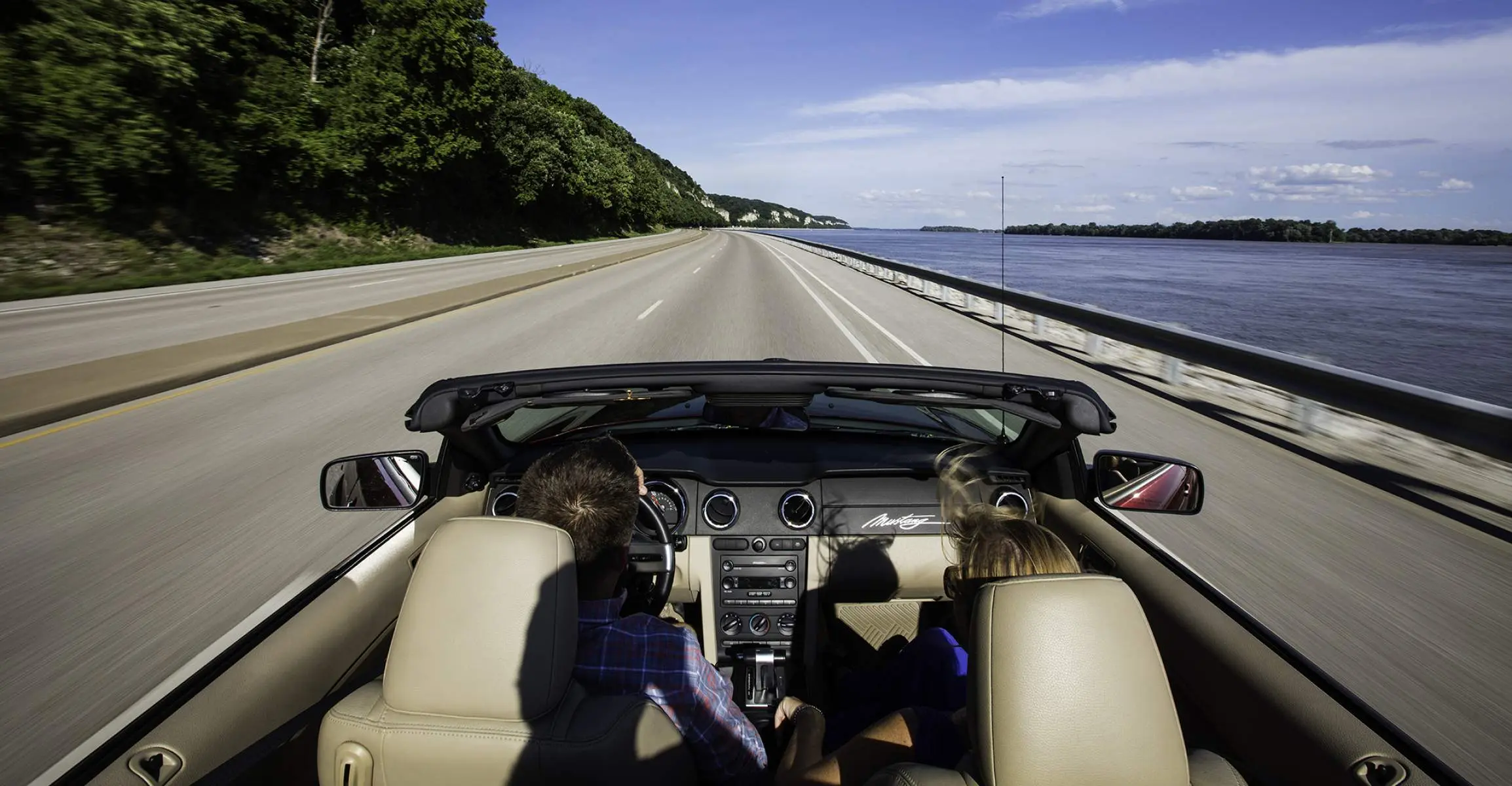 Zwei Personen fahren in einem Auto ohne Dach eine Straße entlang