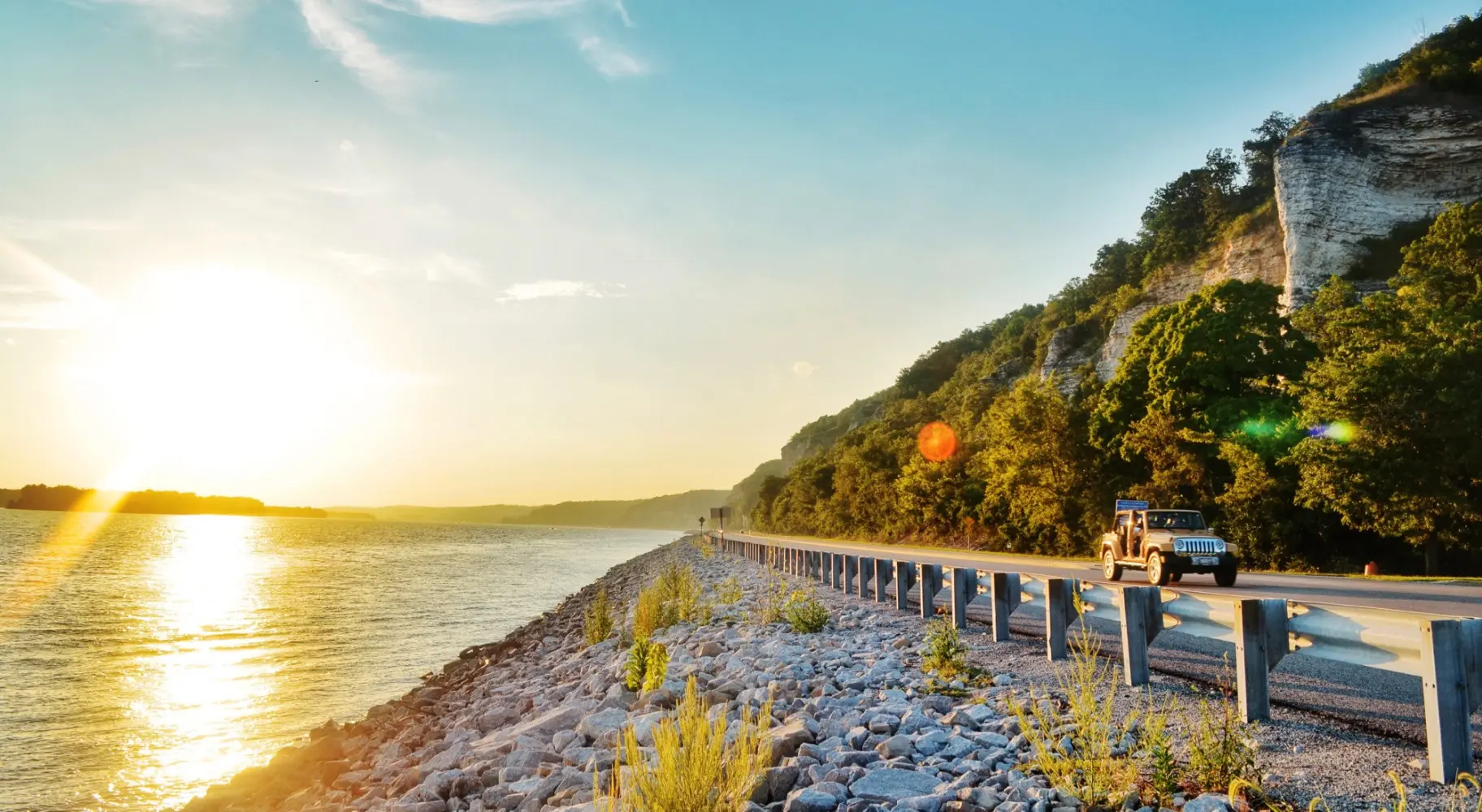 Der Sonnenaufgang über dem Wasser und ein Auto auf der Straße daneben
