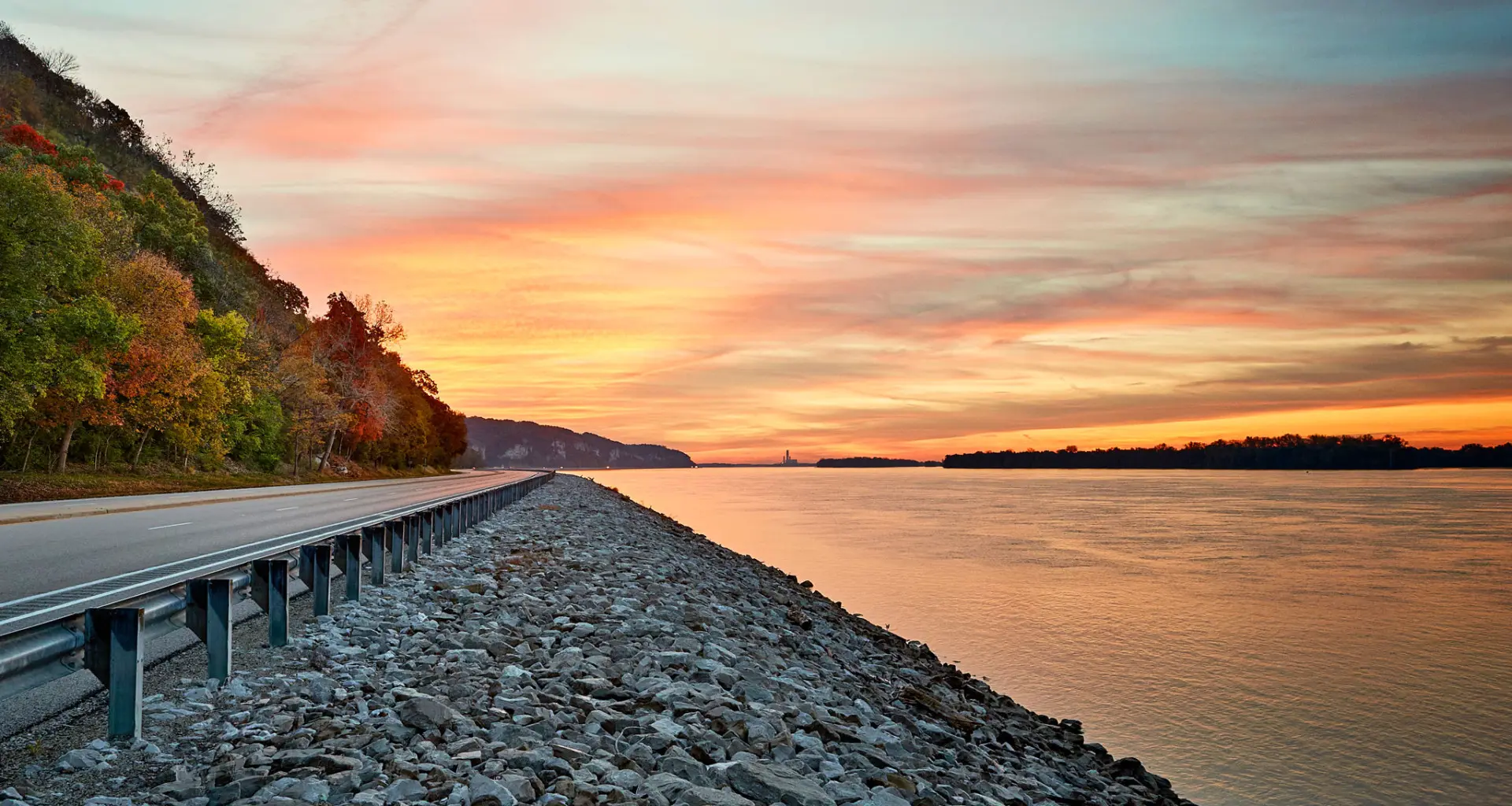 Sonnenuntergang über dem Wasser und einer Straße am Flussufer