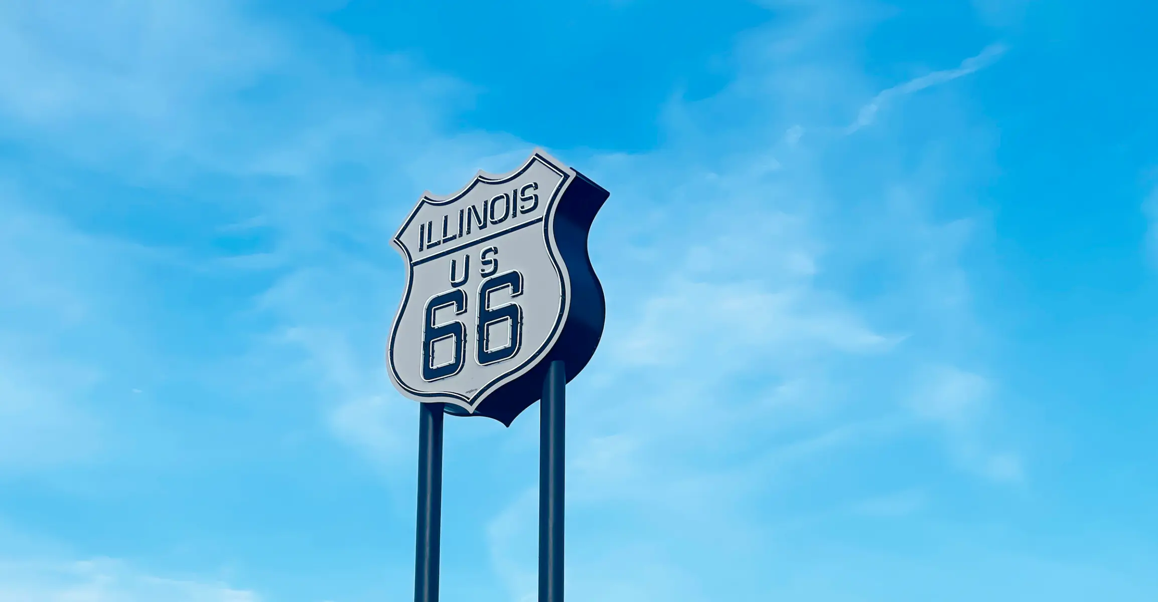 Ein neonfarbenes Route-66-Schild auf zwei Masten vor blauem Himmel