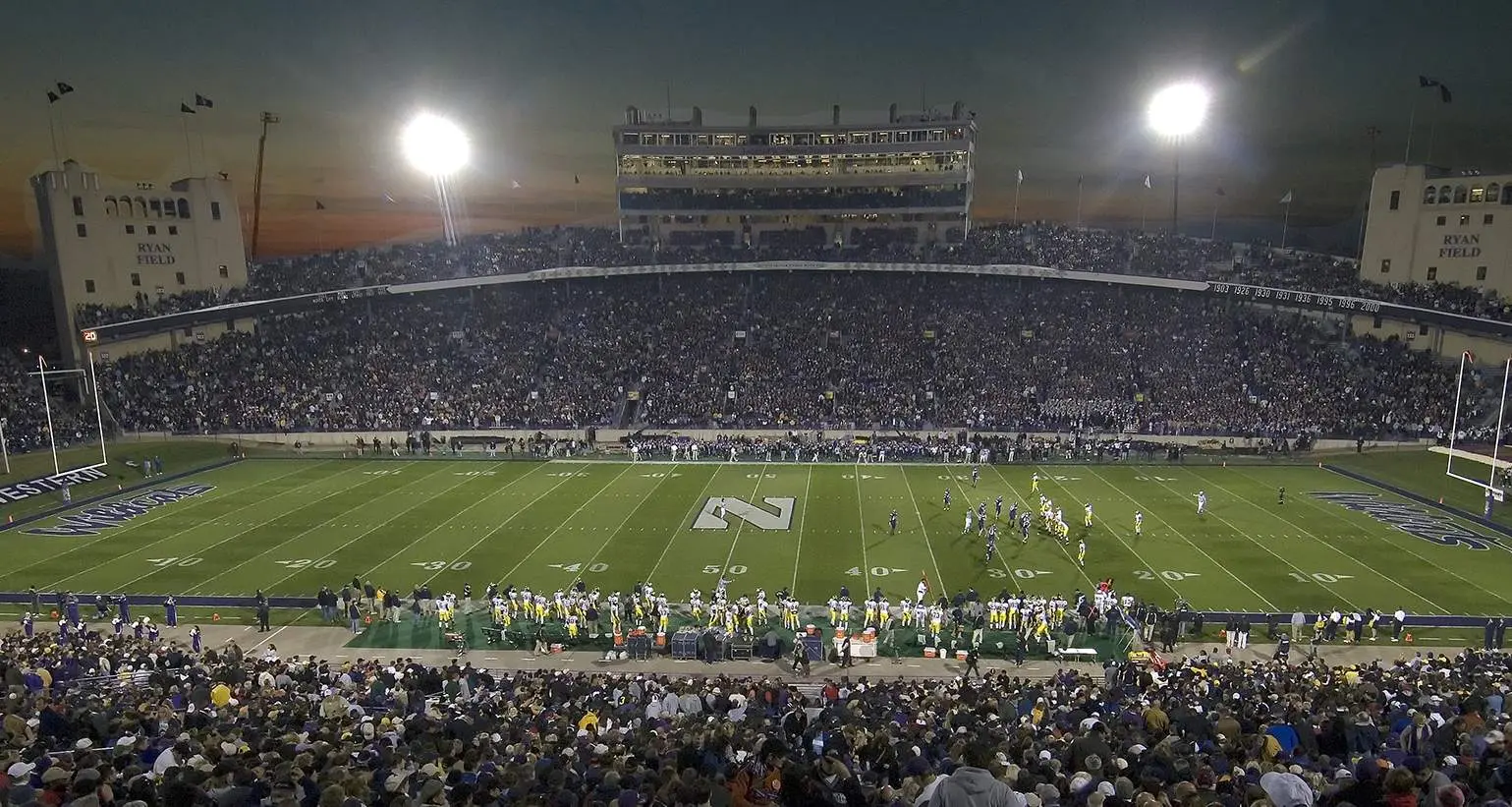 Ein großes College-Football-Stadion am Abend vor einem Spiel, die Tribünen sind voll mit Zuschauern