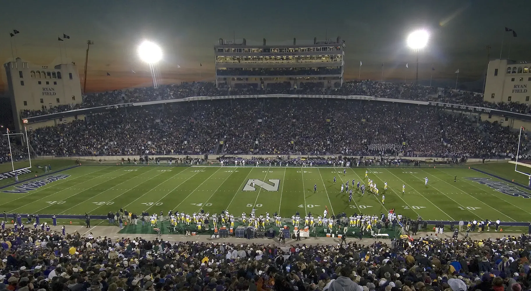 Ein großes College-Football-Stadion am Abend vor einem Spiel, die Tribünen sind voll mit Zuschauern