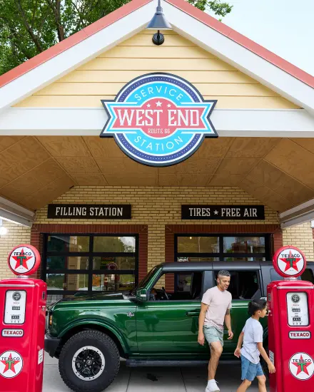 Vater und Sohn gehen an einem grünen SUV und alten Zapfsäulen an der West End Service Station an der Route 66 vorbei.